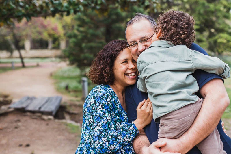 Fotografía familiar en Zaragoza de padres abrazando a su hijo en un parque